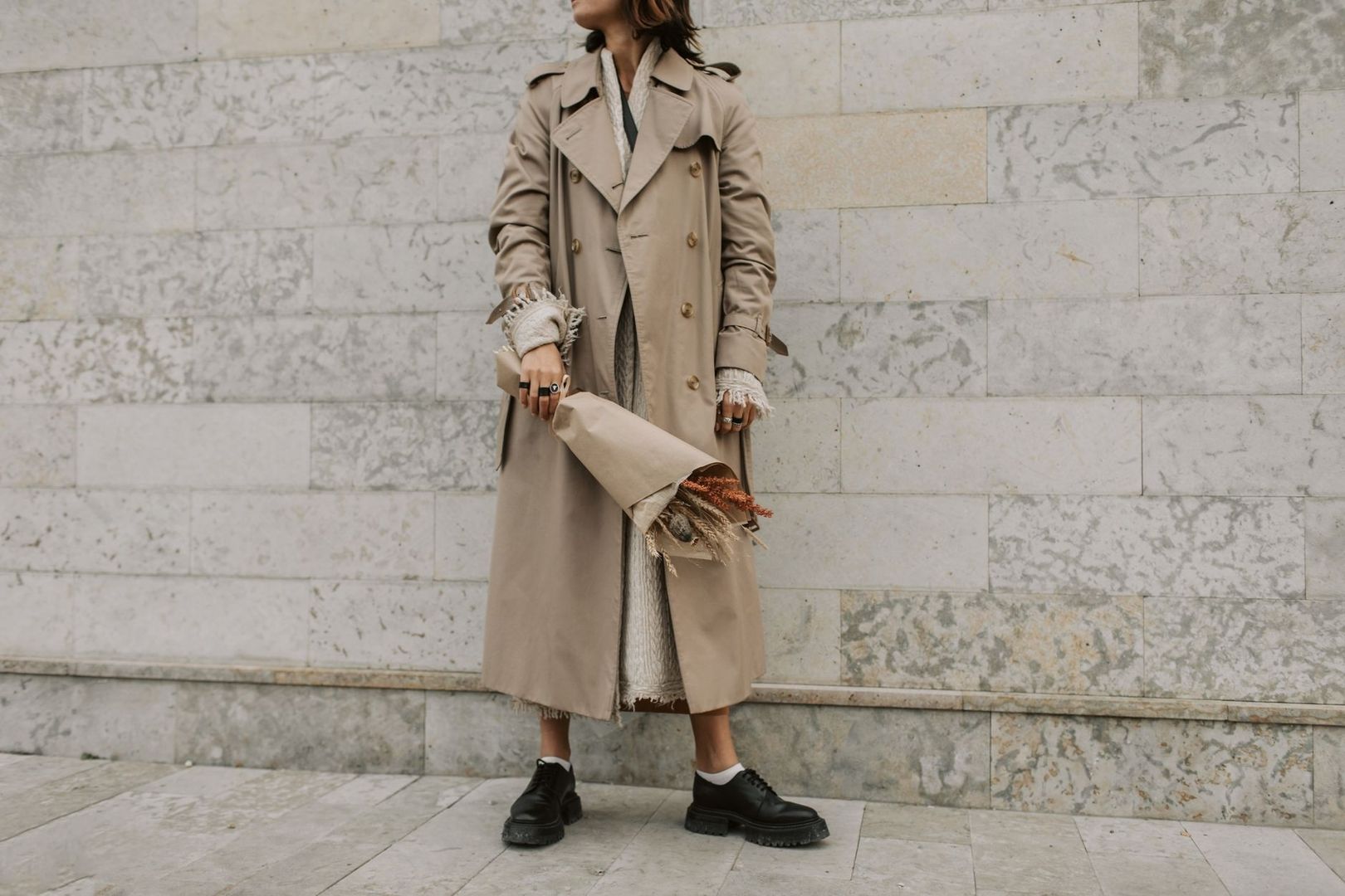 Person i beige trenchcoat med bukett och svarta kraftiga skor