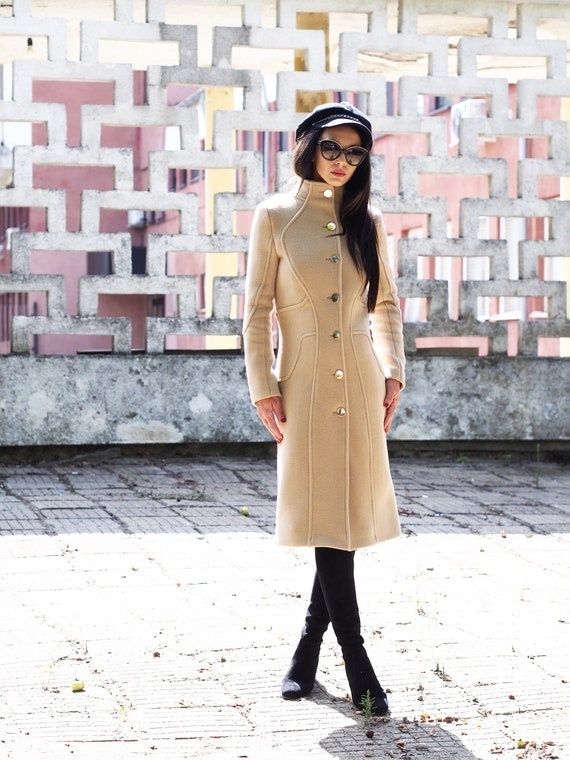 Kvinna i minimalistisk beige ullkappa framför geometrisk vägg