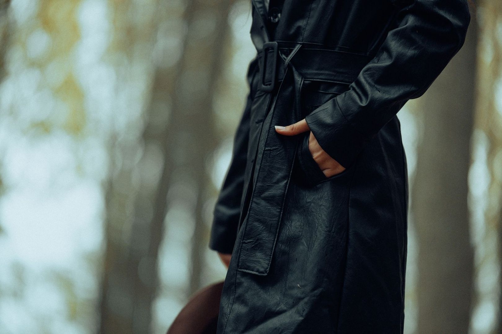 Närbild av svart trenchcoat med bälte och hand i fickan