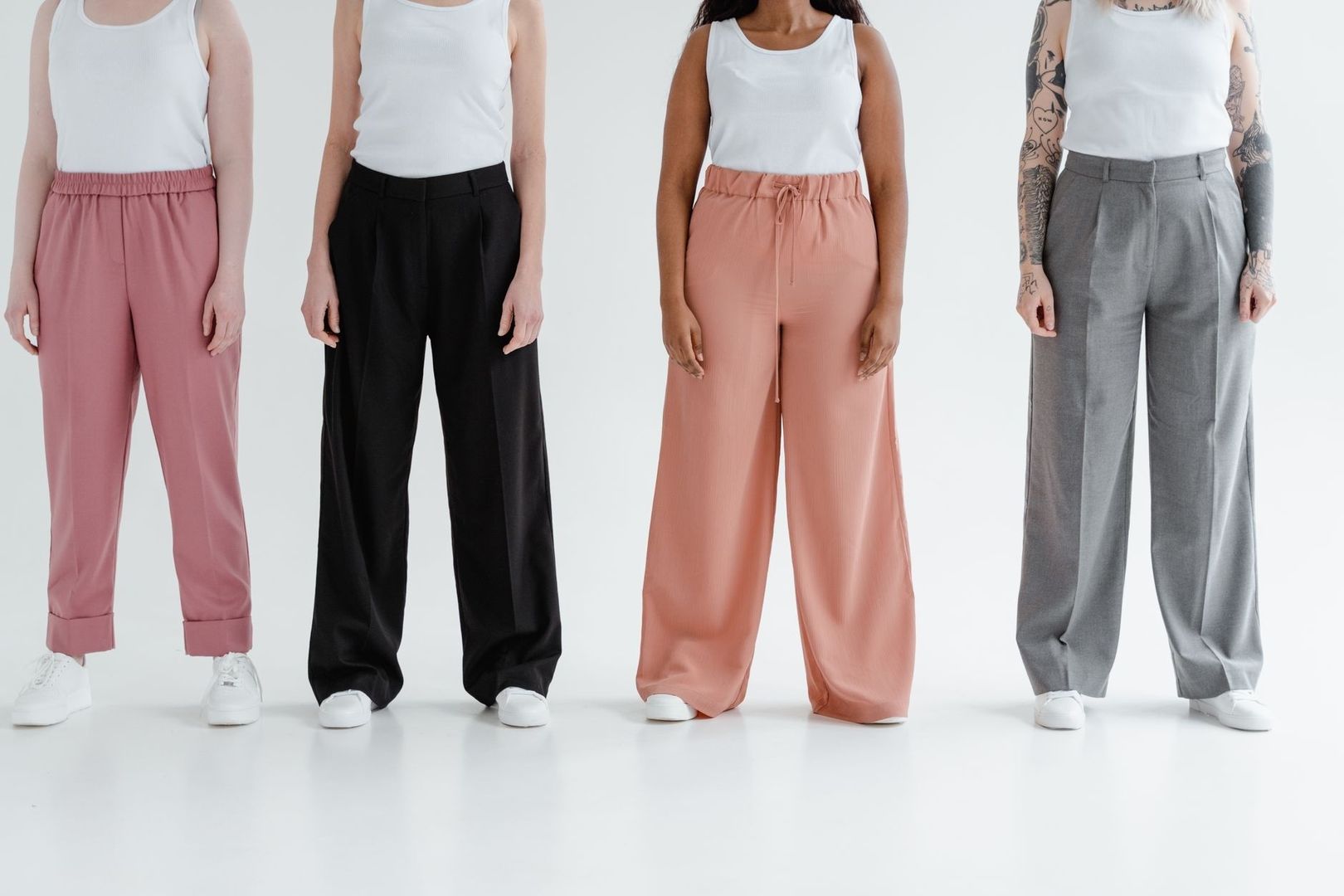 Fyra personer visar högmidjade byxor i rosa, svart och grått
